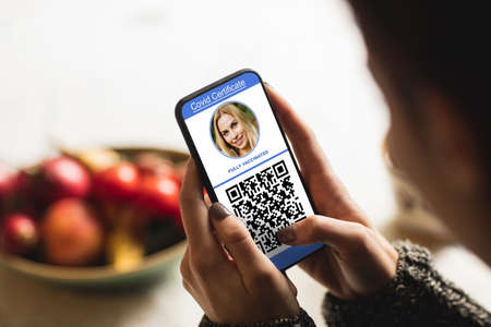 Woman at home holding smartphone with covid 19 vaccine passport. global covid 19 pandemic concept digitally generated video.の写真素材