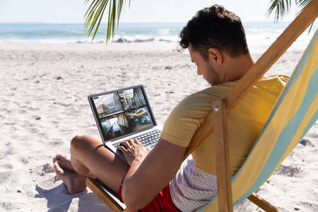 Caucasian man on holidays using laptop with views of offices from security cameras on screen. security, safety, surveillance, and digital interface.の写真素材