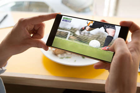 Hands of caucasian man at restaurant watching soccer match on smartphone. sports, competition,...