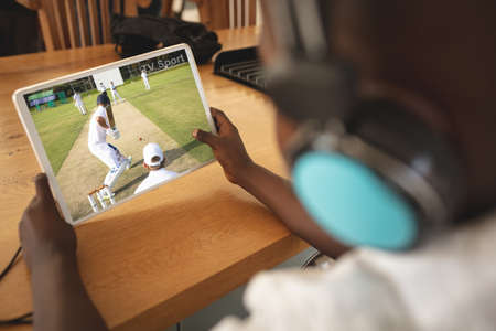 African american boy wearing headphones at home watching baseball game on tablet. sports, competition, entertainment and technology concept digital composite image.の写真素材