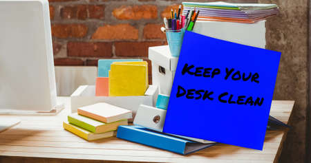 Image of keep your desk clean text on memo note over stationery items on desk. national clean your desk day concept digitally generated image.の写真素材