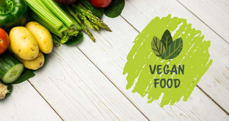 High angle view of vegan food symbol in green by fresh vegetables on white wooden table. digital composite of healthy food and sign.の写真素材