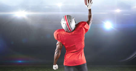 Rear view of male american football player celebrating goal by lifting ball at illuminated stadium. competitive sport and success.の写真素材