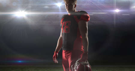 Portrait of confident player wearing jersey holding helmet at illuminated american football stadium. competitive sport and challenge.の写真素材