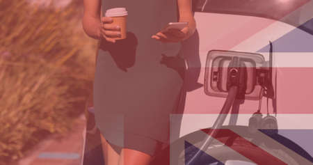 Midsection of woman using smartphone while waiting for electric car at charging station with us flag. digital composite of environmental conservation, transportation and identity.の写真素材