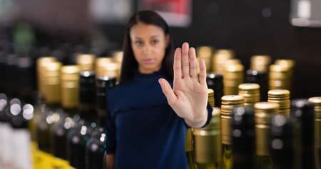 Portrait of young woman showing stop gesture with hand at wine shop. digital composite of lifestyle and alcoholism.の写真素材