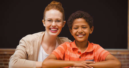 Portrait of smiling redhead teacher sitting with afro student in classroom. education, knowledge and mentorship.の写真素材