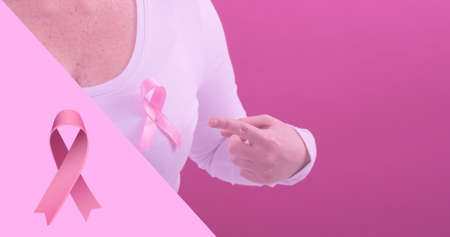 Composition of woman pointing at breast cancer awareness ribbon against pink background, copy space. breast cancer awareness campaign and vector concept.の写真素材