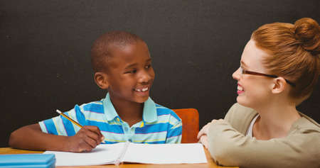 Smiling schoolboy with book and pencil looking at happy redhead teacher in classroom. education, knowledge and mentorship.の写真素材