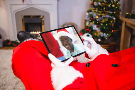 Santa claus making tablet christmas video call with smiling african american boy in santa hat. christmas, festivity and communication technology.の写真素材