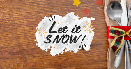 Overhead view of let it snow text over tied cutlery with napkin by stars on wooden table. digital composite of christmas celebration and culture.の写真素材