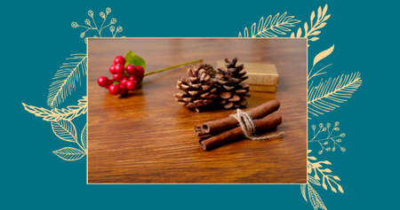 Digital composite of tied cinnamon sticks by pine cones and cherries on table over blue background....