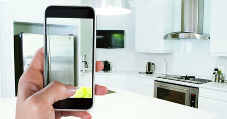 Image of person using smartphone with house kitchen interiors displayed on screen. Online shopping house decorating concept digital composite.の写真素材