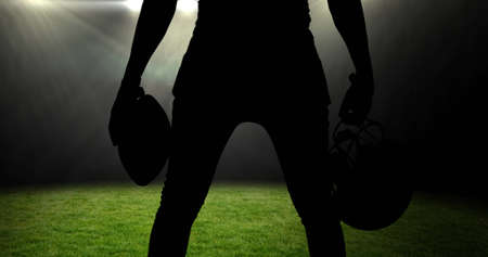 Image of silhouette of american football player holding helmet and ball over sports stadium. sports event and competition concept digitally generated image.の写真素材