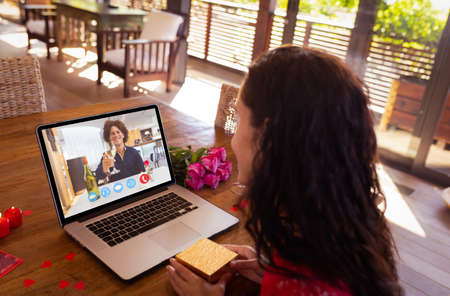 Happy biracial young couple dating on video call through laptop during valentine day. unaltered,...
