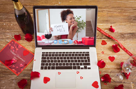Happy african american young woman showing marry me text during online dating on valentine day. unaltered, online dating, video call and distant valentine day celebration.の写真素材