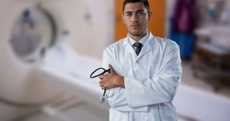 Portrait of confident biracial male doctor with arms crossed standing against mri scanner. copy...