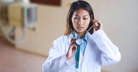 Asian young female doctor examining with stethoscope while standing in hospital. digital composite, copy space, world cancer day, alertness, awareness and hospital concept.の写真素材
