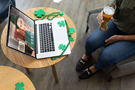 Mid section of woman holding a beer glass while having a video conference on laptop at a bar. st...