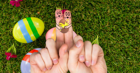 Creative easter bunnies cartoons on index fingers over eggs and grass. digital composite, festive, symbol and creative concept.の写真素材