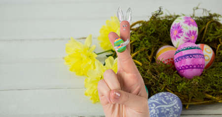 Cropped hand with creative bunny cartoon drawing on crossed fingers over easter eggs in nest....