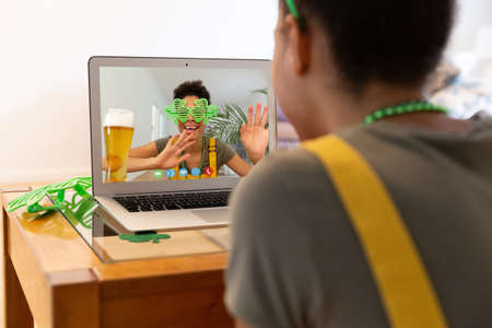 Mixed race woman making st patrick's day video call to friend on laptop at home. celebrating the...