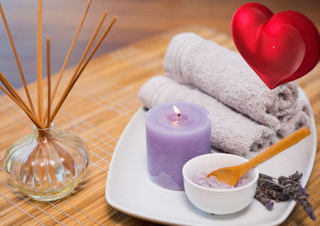 Red heart icon against massage towels, incense towels and candles on wooden table. beauty spa conceptの写真素材