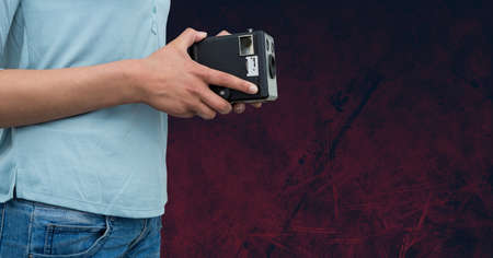 Mid section of a man holding a retro camera against copy space on grunge textured red background. photography conceptの写真素材