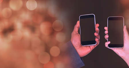 Composition of light circles over two diverse male and female hands holding smartphones. global...