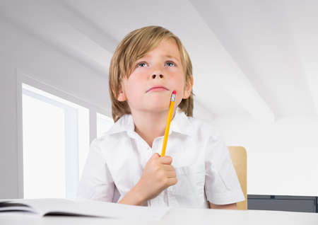 Thoughtful caucasian boy holding a pencil at school against office in background. school and education conceptの写真素材