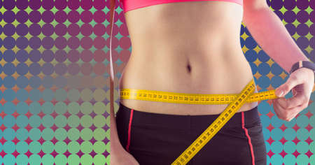 Mid section of caucasian fit woman measuring her waist against colorful background with copy space. sports and fitness conceptの写真素材