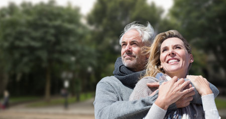 Smiling caucasian senior man embracing senior woman against trees in park during sunny day. love, togetherness, lifestyle, unaltered, senior citizens, retirement and awareness concept.の写真素材