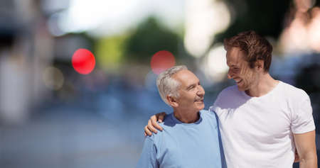 Smiling caucasian mid adult man with senior father standing against defocused background in city....