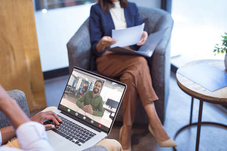 Smiling african american businessman video conferencing with female colleague through laptop. unaltered, office, online, wireless technology, discussion, internet, business, teamwork.の写真素材