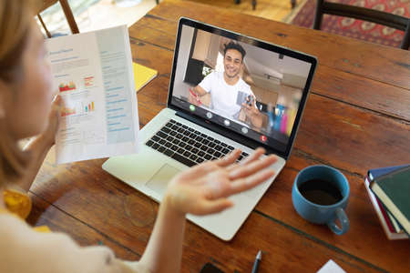 Asian businesswoman discussing graphs and report with male colleague on laptop in office. unaltered, online, wireless technology, video conference, discussion, internet, business, teamwork.の写真素材