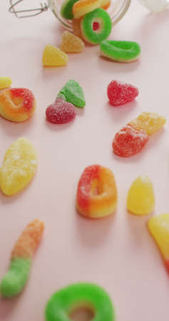 Vertical image of jelly candy spilling out of glass jar on pink background. sweet foods and candy.