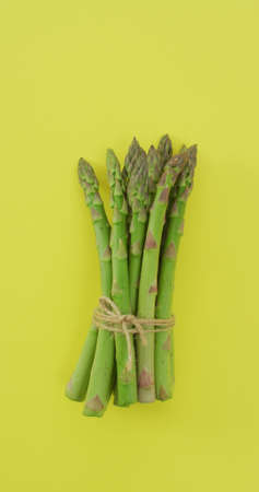 Vertical image of fresh stalks of asparagus tied with rustic string on yellow background. fresh and organic vegetable produce.の写真素材