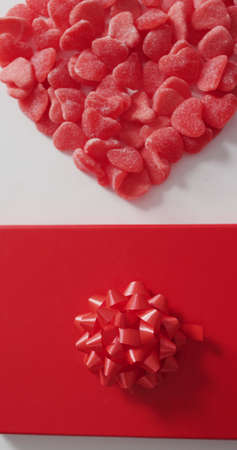 Vertical image of overhead view of red candies in heart shape, and wrapped gift on white....