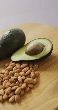 Vertical image of almonds and whole and halved avocado on wooden table with lilac background....