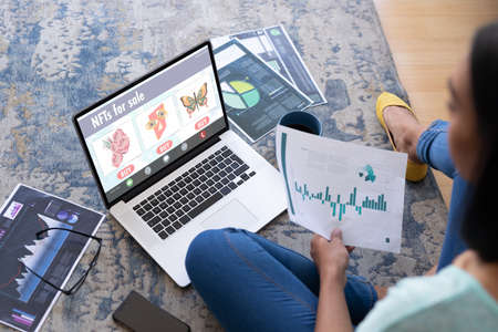 Asian woman studying graphs while researching on nfts through laptop at home. unaltered, business, freelancer, technology, non fungible tokens, finance.の写真素材
