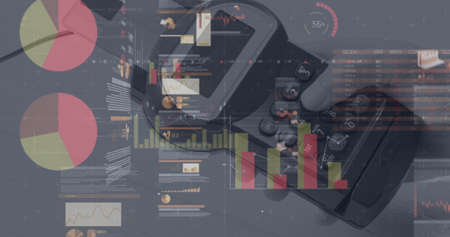 Image of graphs and financial data over hand of caucasian man holding payment terminal. finance,...