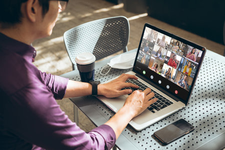 Asian businessman using laptop in cafe during video conference with multiracial colleagues. unaltered, wireless technology, business, drink, covid-19, working and office concept.の写真素材
