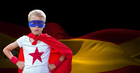Caucasian boy in superhero costume against waving spanish flag with copy space on black background. spanish patriotism and sport conceptの写真素材