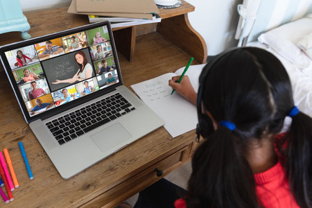 Biracial girl writing english notes in book while learning from online class over video call at home. Screen, unaltered, childhood, wireless technology, education, student and e-learning concept.の写真素材