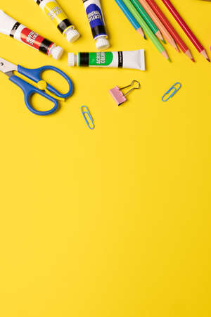 Imagine of various office supplies and plastic utensils, paints, crayons on yellow background. Education, learning and creativity.の写真素材