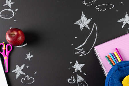 Image of school supplies, apple and notebook over drawings on black board. Education, learning and creativityの写真素材