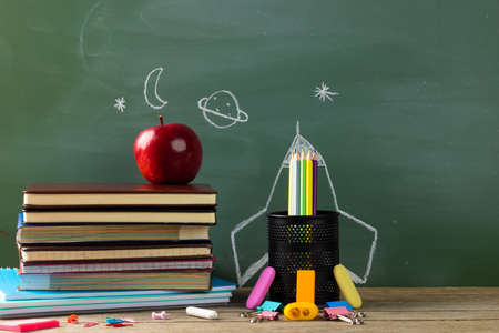 Image of school supplies, apple and notebook over drawings on black board. Education, learning and...