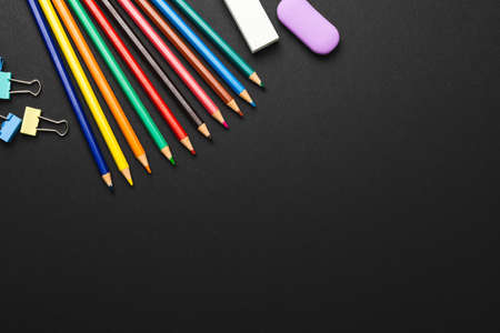 Composition of colorful crayons and school items on black surface with copy space. School equipment,...