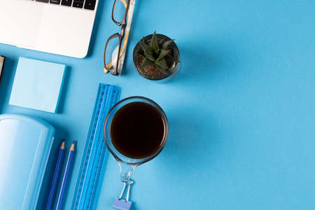 Image of various office supplies, paper and cup of black coffee on blue background. Education,...