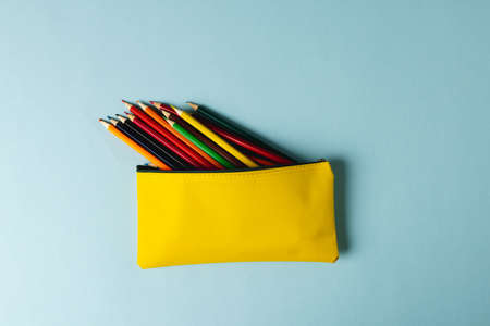 Composition of colorful crayons in yellow case on mint surface with copy space. School equipment,...